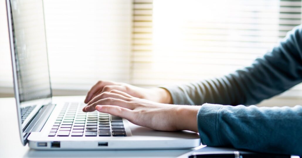 Hands typing an email on a laptop at a bright desk