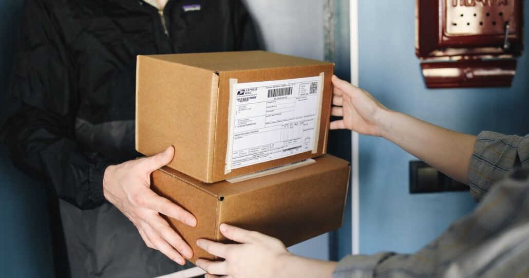 A courier handing over two labelled shipping boxes at a front door