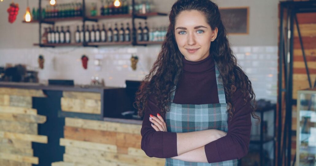A smiling cafe owner with her arms crossed behind the counter of her shop