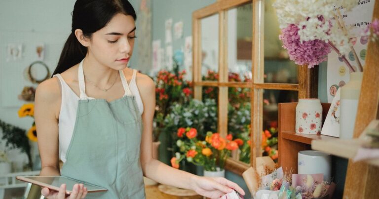 A florist in an apron checking her store on a tablet among bouquets